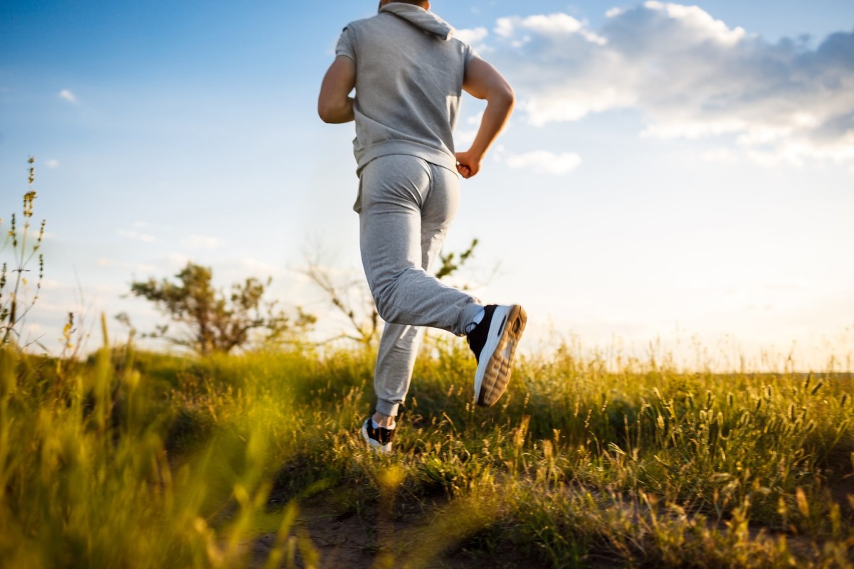 Close up of sportive man jogging in field at sunrise.
